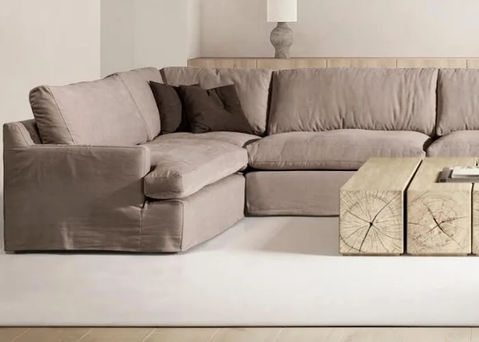 Sofá Upi en rinconera con funda en tono topo y cojines marrones, junto a una mesa baja de troncos de madera