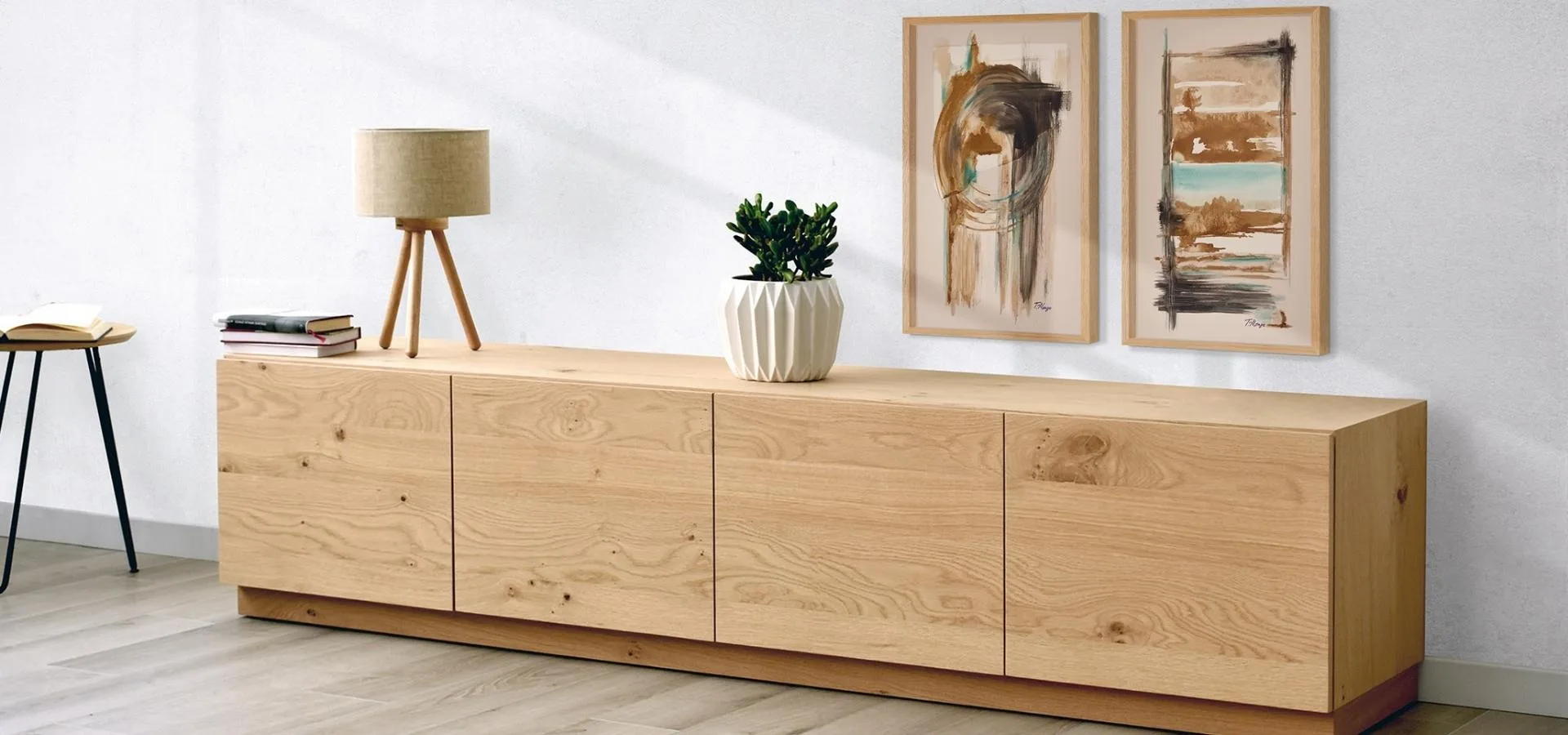 Dos cuadros abstractos en marrón y ocre sobre un mueble bajo de madera clara, con lámpara de trípode