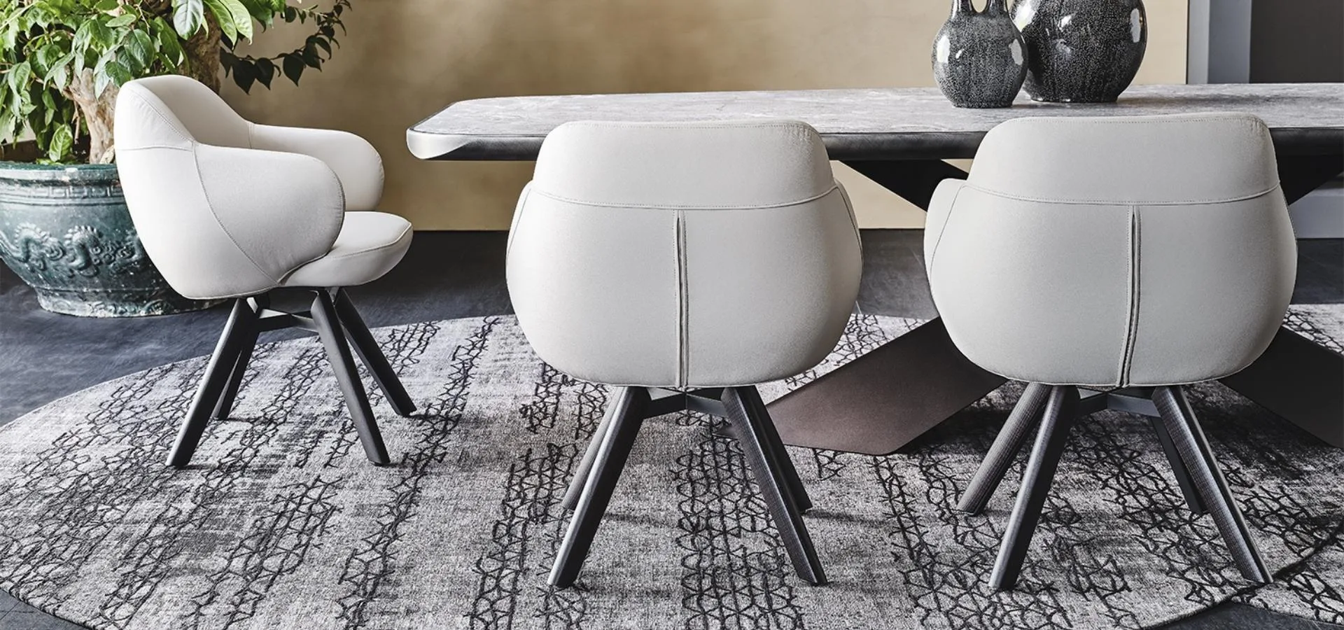 Comedor con tres sillas tapizadas en gris claro y patas oscuras abiertas alrededor de una mesa sobre alfombra gris
