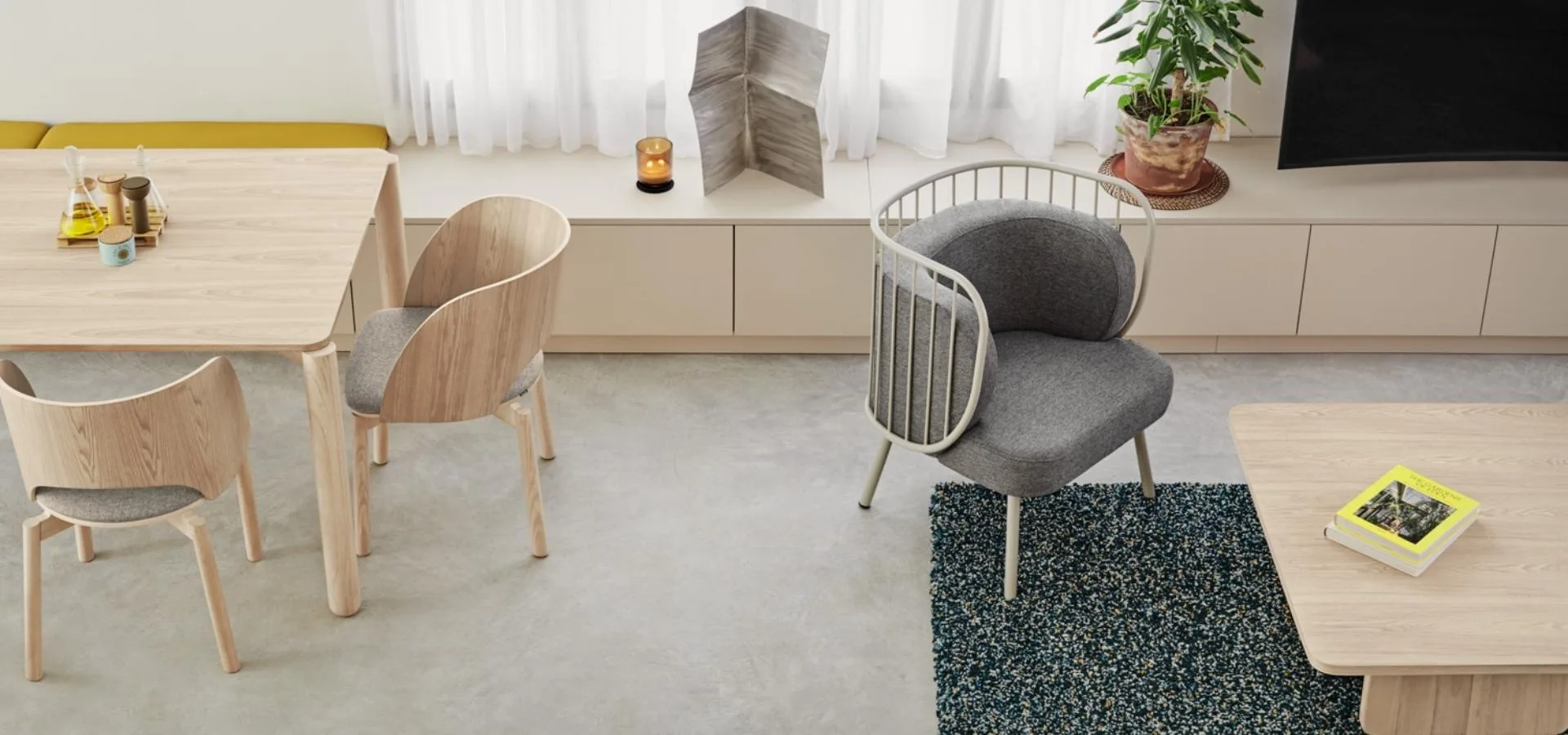 Comedor con mesa y sillas de madera clara, una butaca gris de respaldo de varillas y un mueble bajo blanco
