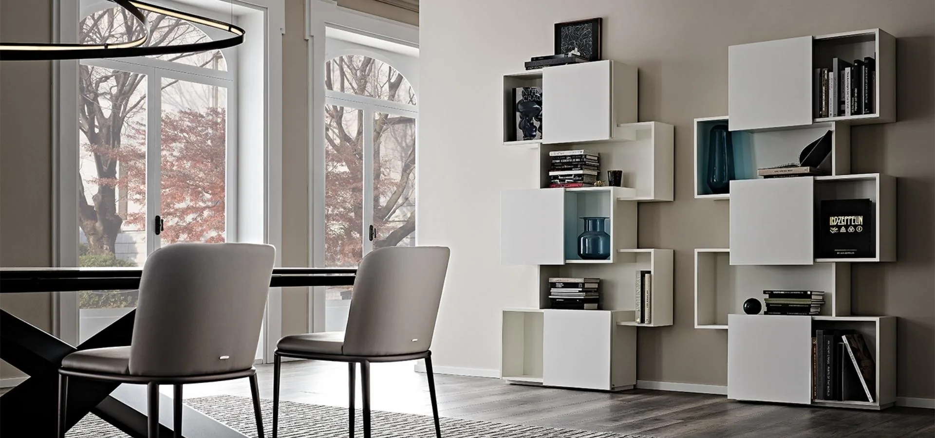 Estantería modular blanca con cubos abiertos junto a un comedor con sillas tapizadas y ventanales