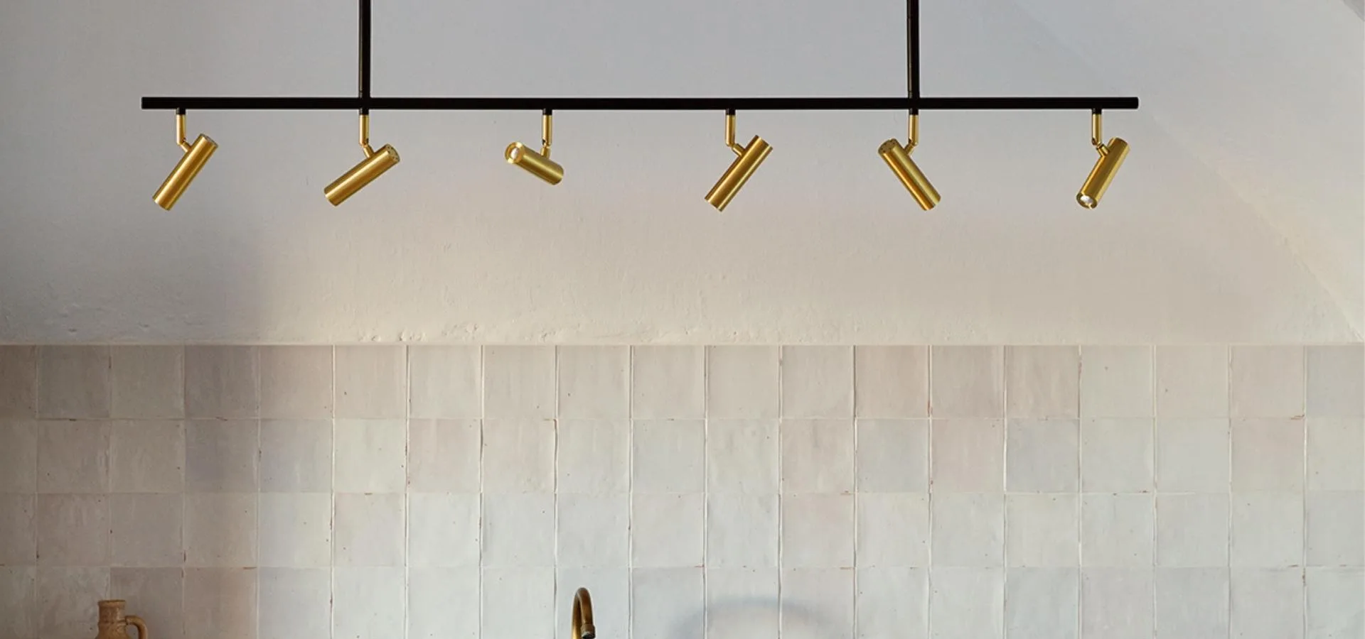 Lámpara de techo con barra negra y seis focos dorados sobre una pared de azulejos blancos