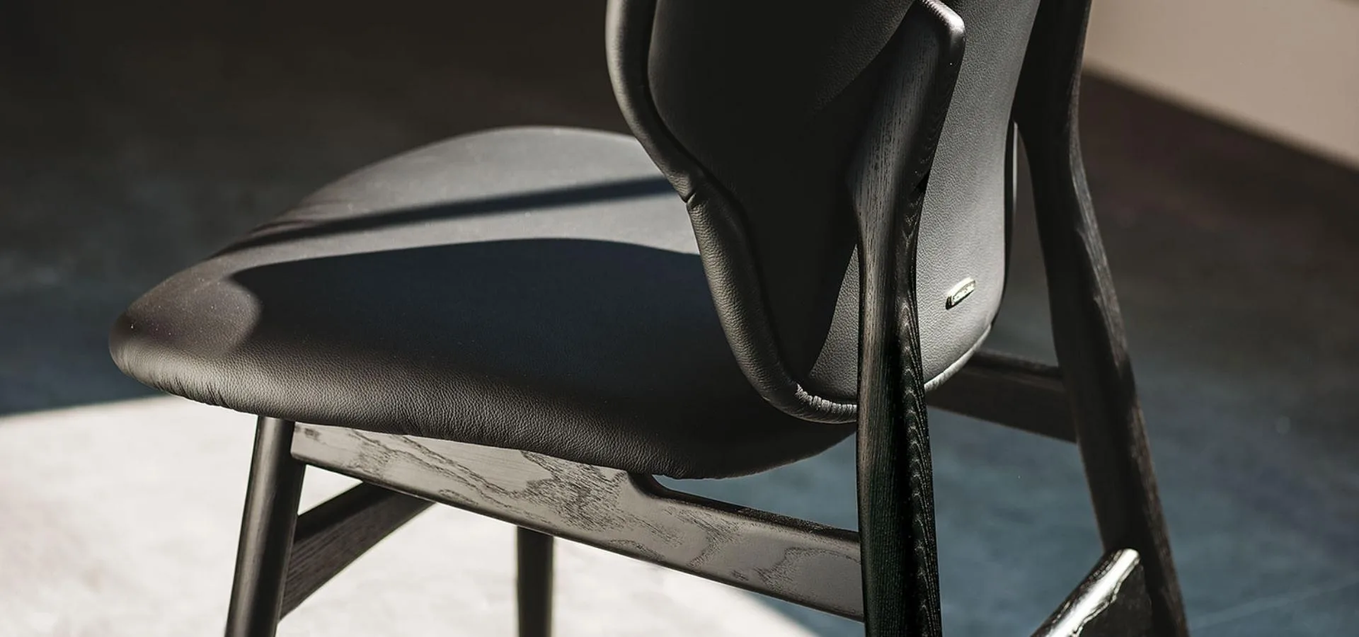 Detalle de una silla negra con asiento y respaldo tapizados y estructura de madera oscura con costuras visibles