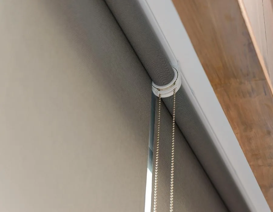 Detalle del lateral de un estor enrollable gris con su cadena metálica de accionamiento