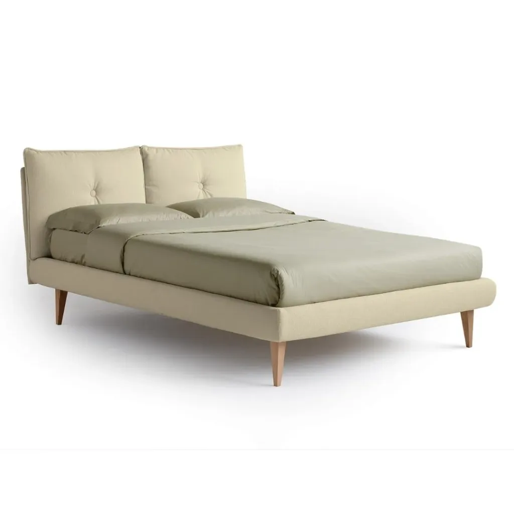 Cama tapizada en beige con cabecero de dos cojines abotonados y patas de madera inclinadas