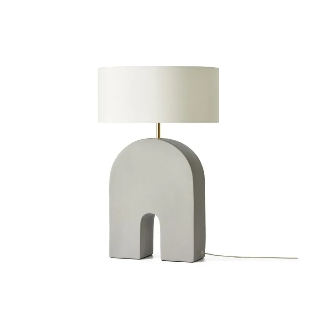 Lámpara de mesa con pie gris en forma de arco y pantalla blanca de tambor, sobre fondo blanco