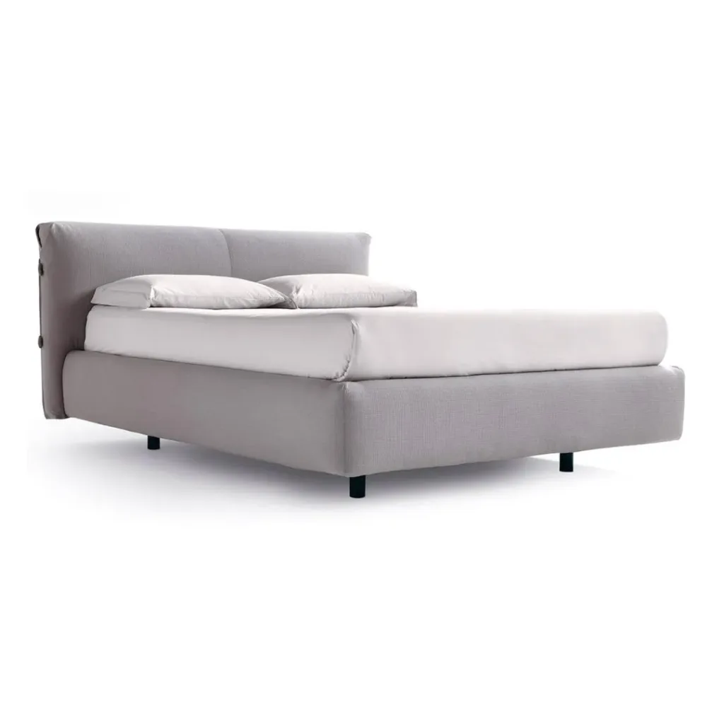 Cama tapizada en gris perla con cabecero bajo y recto, cojines blancos y patas negras cortas