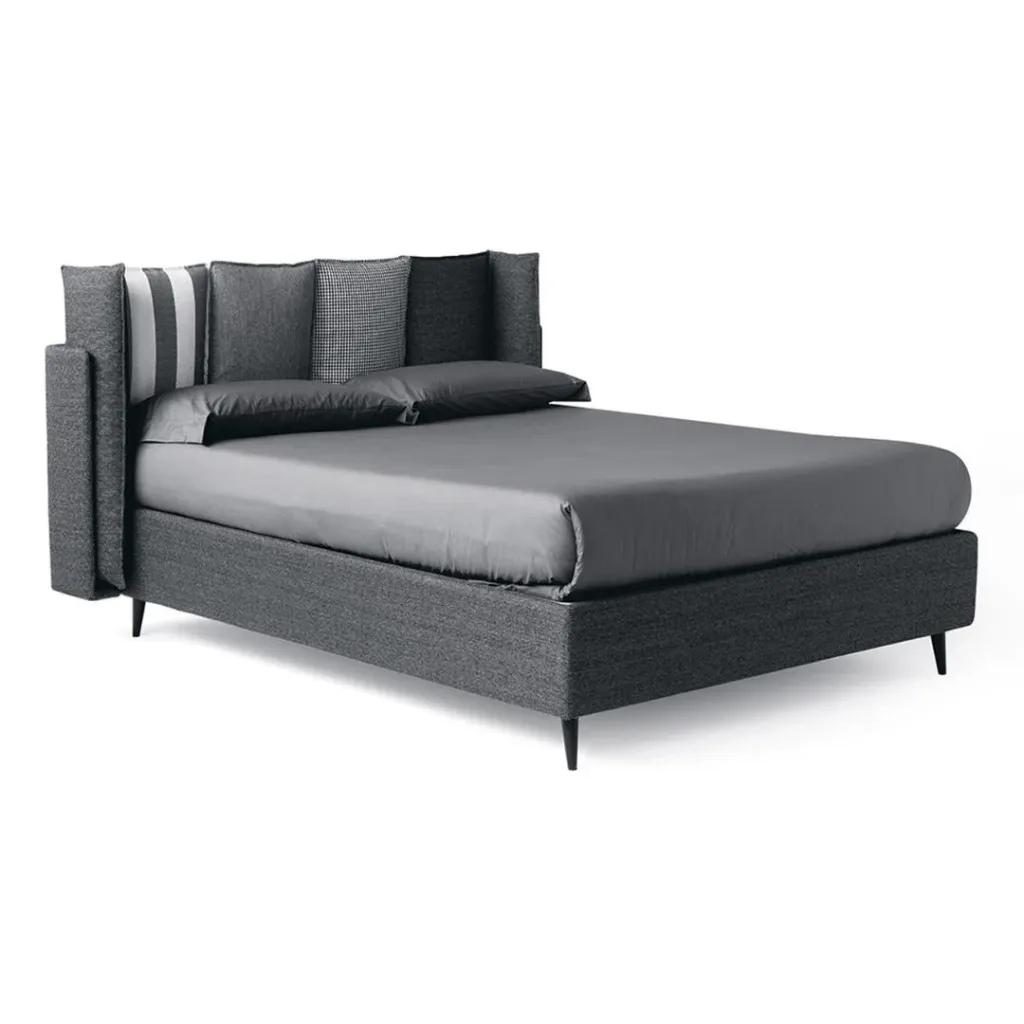 Cama tapizada en gris marengo con cabecero de cojines, uno a rayas blancas, y un lateral acolchado