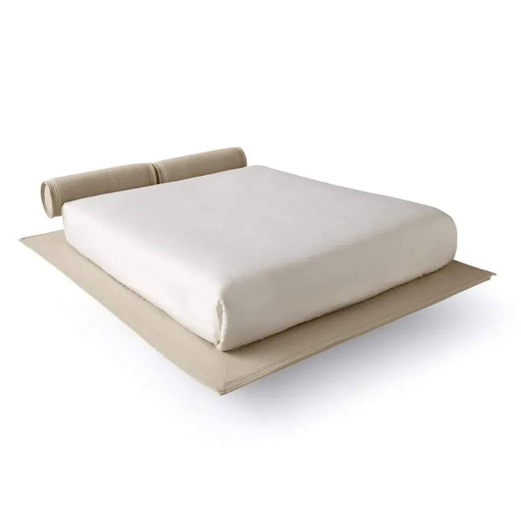 Cama baja sin cabecero, con dos cojines cilíndricos como respaldo sobre una base beige que sobresale
