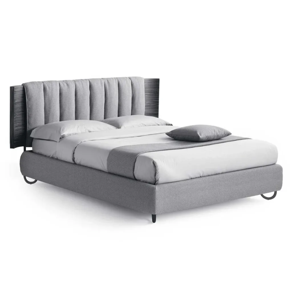 Cama con base tapizada gris y cabecero de canales verticales sobre panel oscuro, con patas curvas