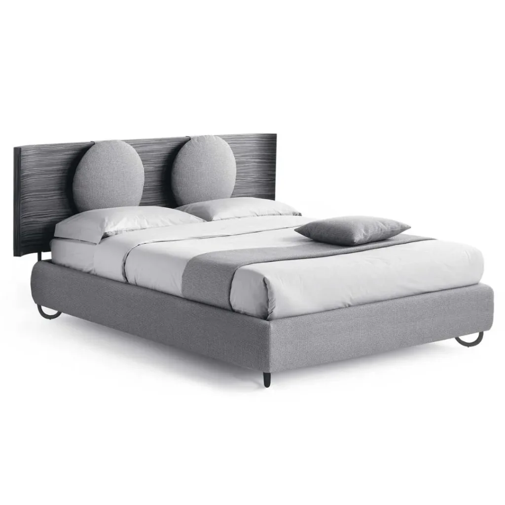 Cama con base tapizada gris y cabecero oscuro con dos cojines redondos grises