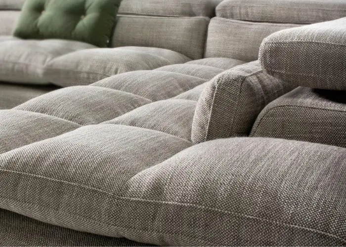 Asientos acolchados del sofá Irohito en detalle, con tejido gris texturizado y un cojín verde