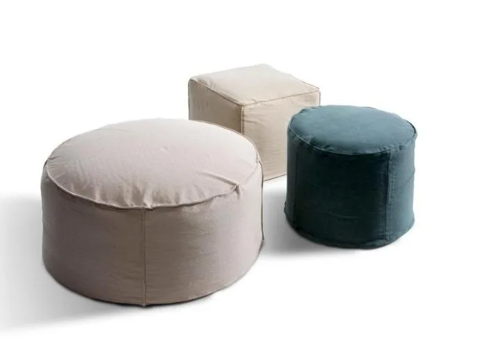 Pufs Arka de cerca: redondo bajo en beige delante, cubo crema y cilindro azul petróleo detrás