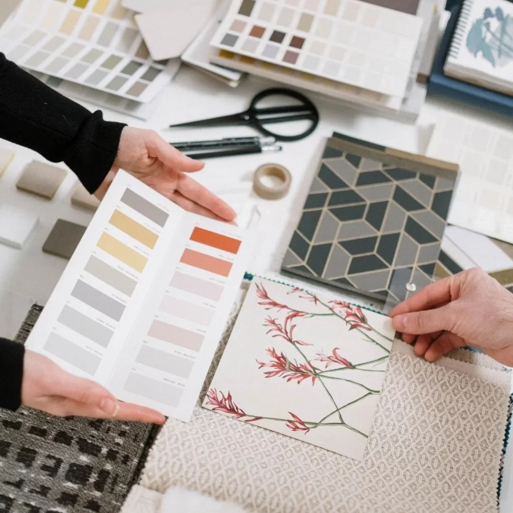 Manos mostrando una carta de colores y muestras de tela estampada sobre una mesa con tijeras y muestrarios